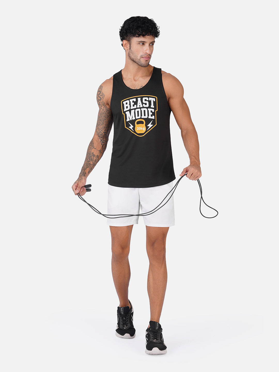 A man modeling a black tank top with a 'BEAST MODE' graphic, paired with white athletic shorts and black sneakers, holding a jump rope against a light gray background.