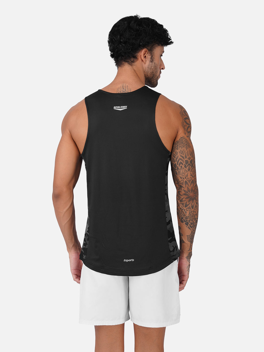 A man shown from the back wearing a black sleeveless athletic tank top and white shorts against a light gray studio background.