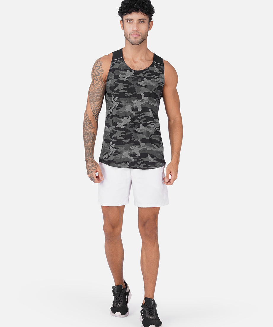 A man modeling a sleeveless athletic tank top with a dark gray and black camouflage pattern, paired with white shorts and black sneakers, against a light gray studio background.