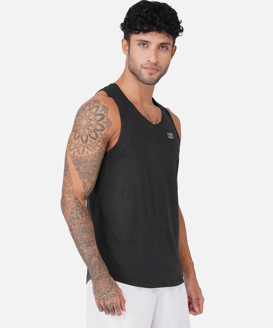 A man wearing a black ribbed athletic tank top and white shorts, standing against a light gray studio background.