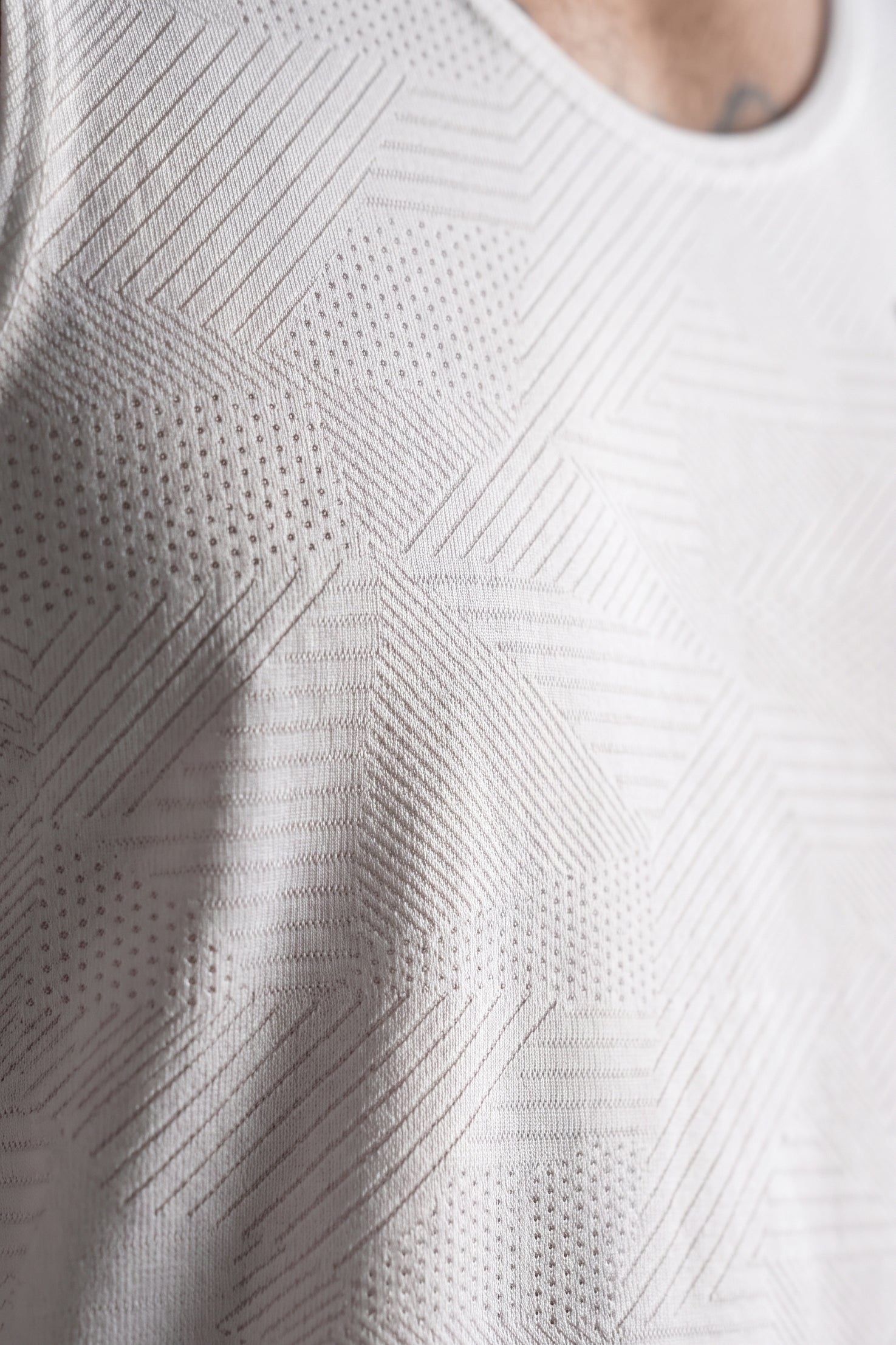 Close-up of a white textured knit top with a geometric diamond pattern and perforated details, worn by a model.