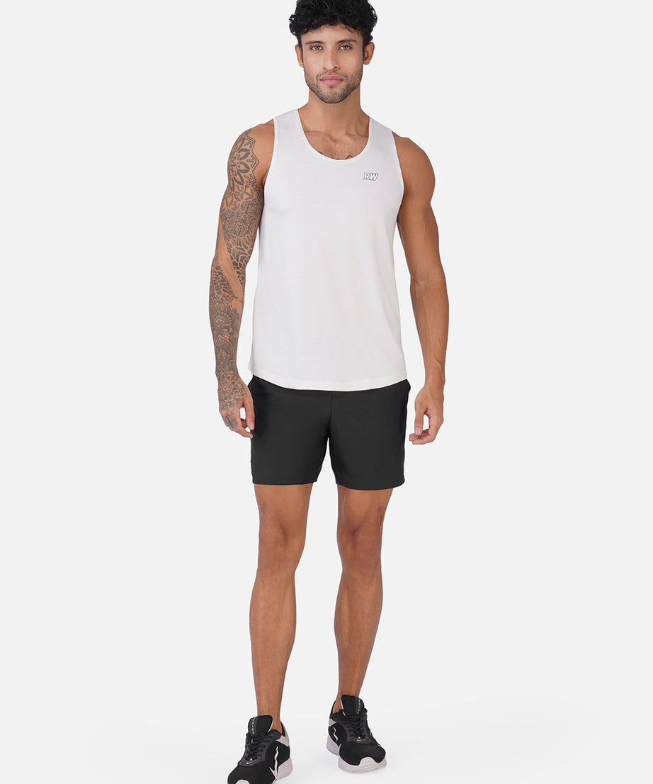 A man modeling a white sleeveless athletic tank top and black athletic shorts against a light gray studio background.