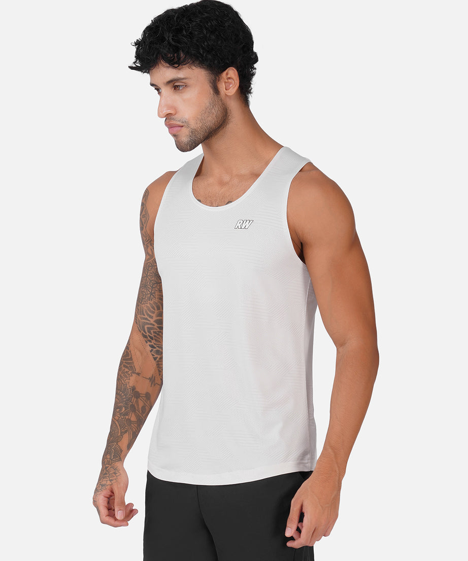 A man wearing a white sleeveless athletic tank top with a small logo on the left chest, paired with black athletic pants, photographed against a light gray studio background.