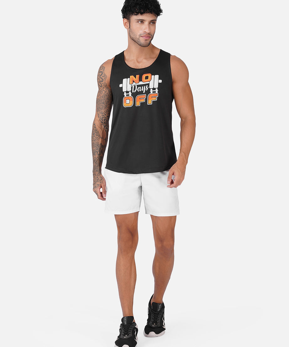 A man modeling a black sleeveless tank top with a white and orange graphic that reads 'No Days Off' with barbell details, paired with white shorts and black sneakers, against a light gray studio background.