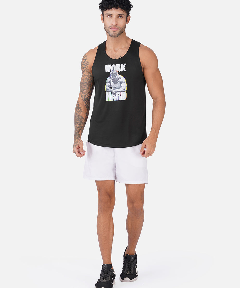A man modeling a black sleeveless tank top with a white and gray graphic that reads 'WORK HARD' on the front, paired with white athletic shorts and black sneakers, against a light gray studio background.