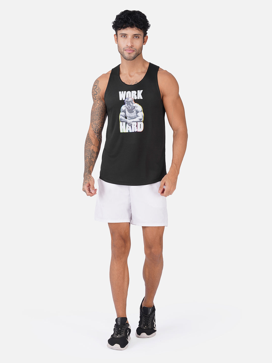 A man modeling a black sleeveless tank top with a white and gray graphic that reads 'WORK HARD' on the front, paired with white athletic shorts and black sneakers, against a light gray studio background.