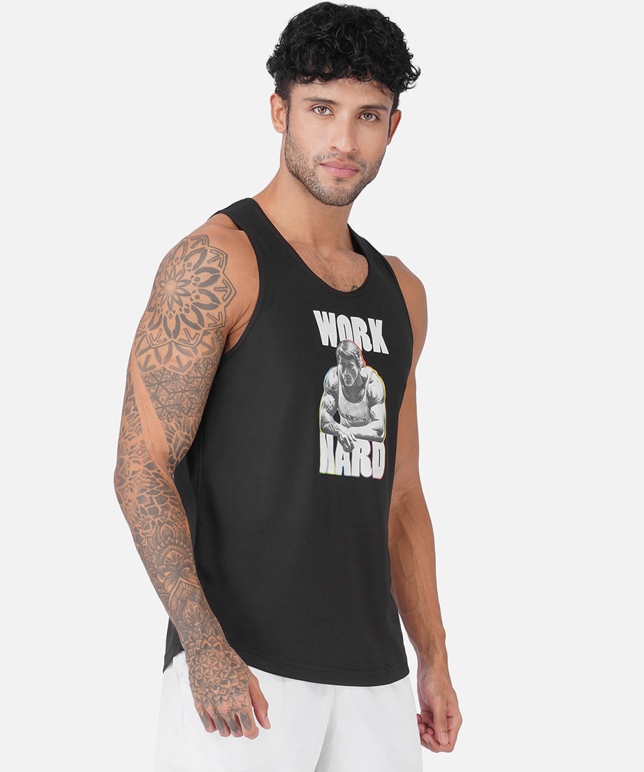 A man wearing a black sleeveless tank top with a white graphic print that reads 'WORK HARD' and a photo of a muscular man, paired with white pants, against a light gray background.