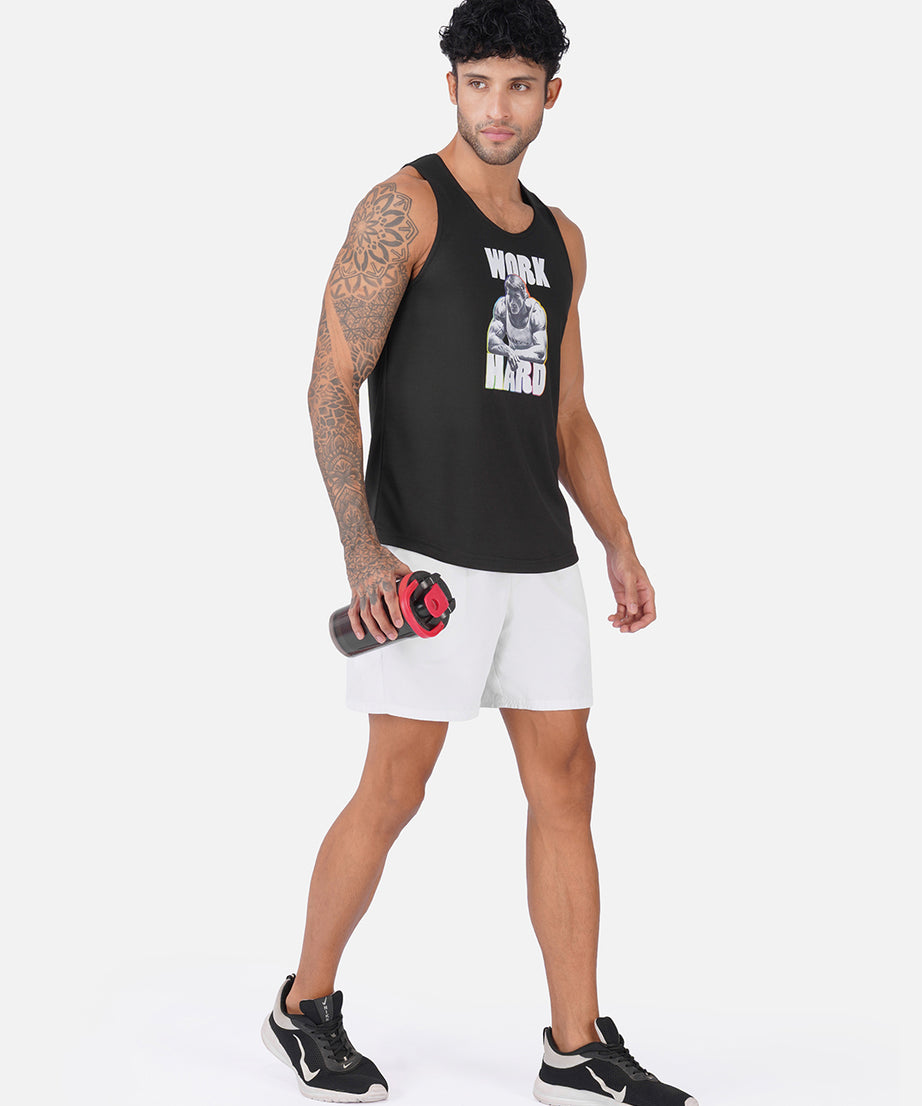 A man modeling a black sleeveless tank top with a white graphic print that reads 'WORK HARD' and a skull graphic, paired with white athletic shorts and black sneakers, holding a water bottle against a light gray studio background.