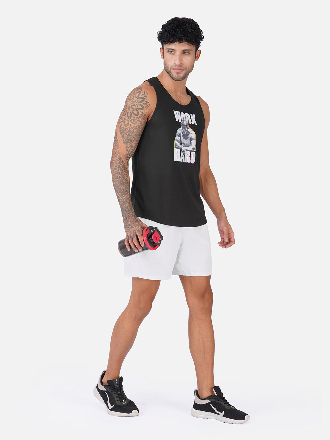 A man modeling a black sleeveless tank top with a white graphic print that reads 'WORK HARD' and a skull graphic, paired with white athletic shorts and black sneakers, holding a water bottle against a light gray studio background.