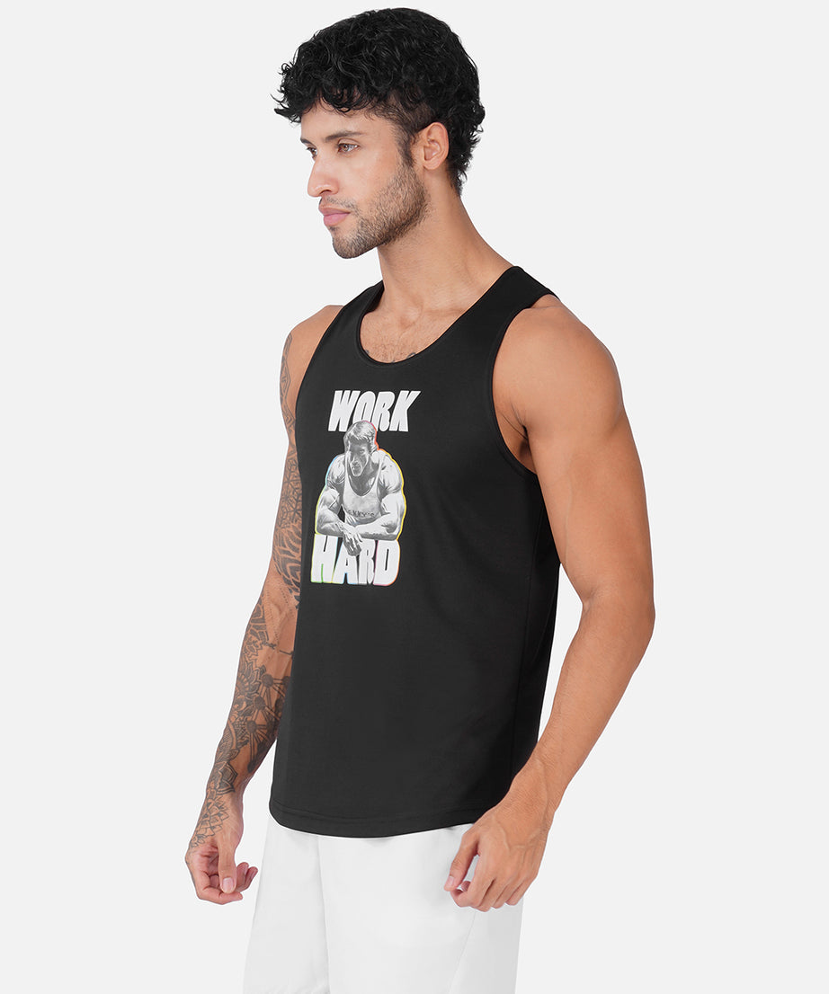 A man wearing a black sleeveless tank top with a white and gray graphic print that reads 'WORK HARD' and white athletic shorts, photographed against a light gray studio background.