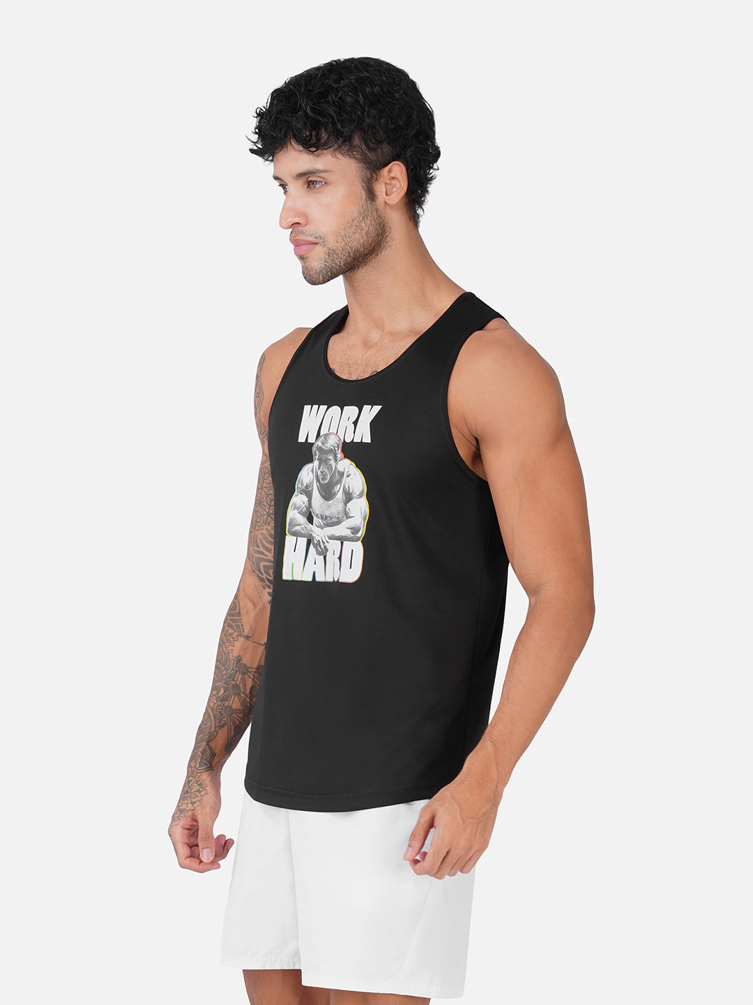 A man wearing a black sleeveless tank top with a white and gray graphic print that reads 'WORK HARD' and white athletic shorts, photographed against a light gray studio background.